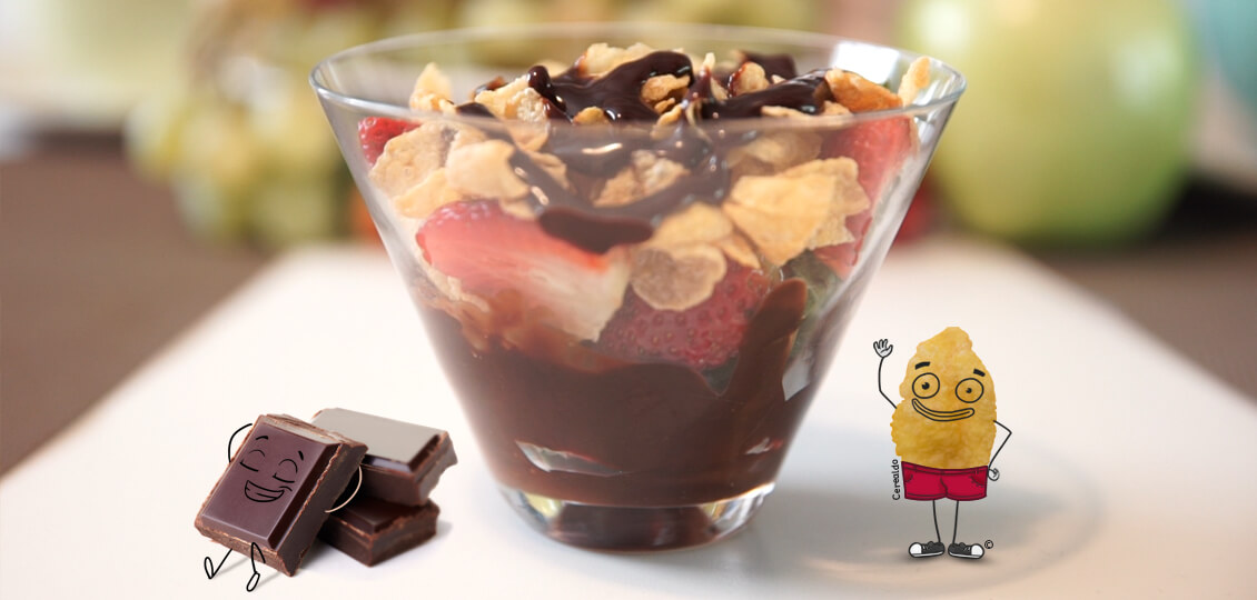 Cerealdo junto a un vaso lleno de fresas, hojuelas y chocolate.